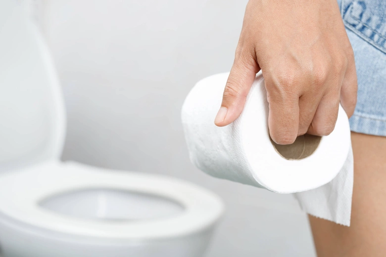 Ruka drží toaletní papír před záchodem v koupelně.