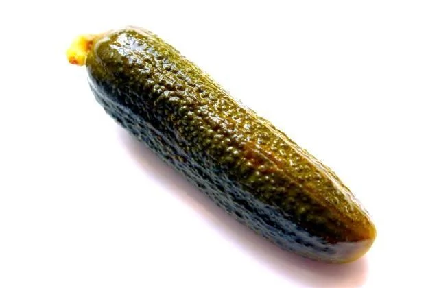 Zelená okurka salátová v solném nálevu na bílém pozadí.