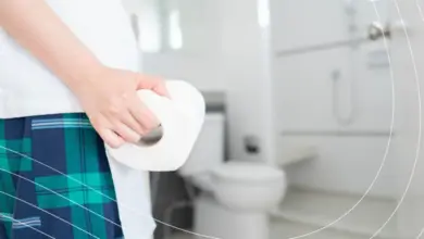 Osoba drží toaletní papír v koupelně.