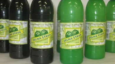 Řada lahví zelené šťávy zelné s viditelnými štítky na světlém povrchu.