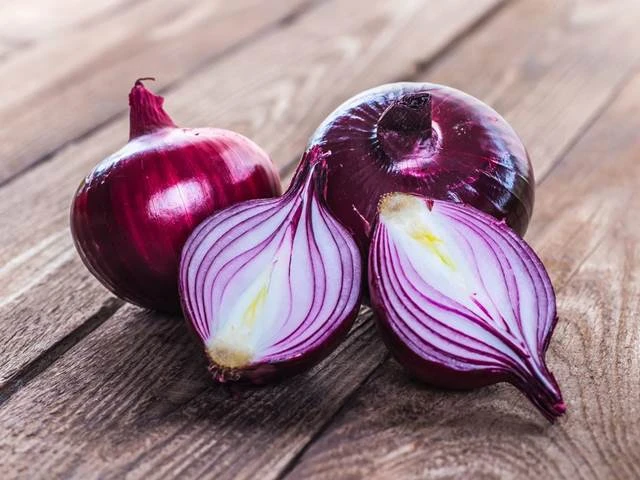 Červené cibule na dřevěném povrchu pro článek o kašli.
