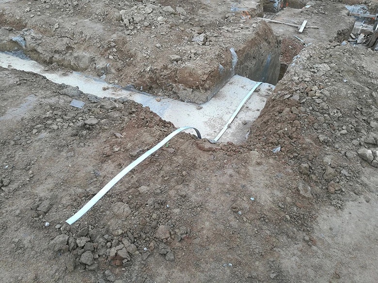 Bílý uzemňovací vodič položený v jámě u základové desky.