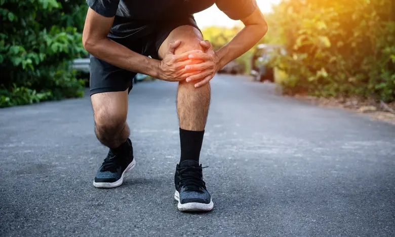 Muž drží bolestivé koleno po sportování venku.