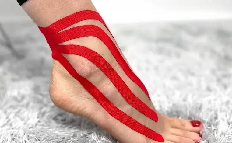 Červená kinéziotape na kotníku při léčbě podvrtnutí