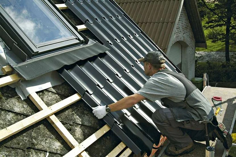 Stavebník montuje tmavý falcovaný plech na střechu.