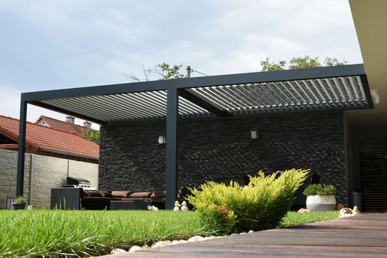 Moderní černá kovová pergola nad zahradním posezením.