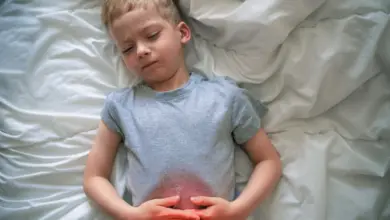 Dítě leží v posteli a drží si břicho kvůli bolesti.