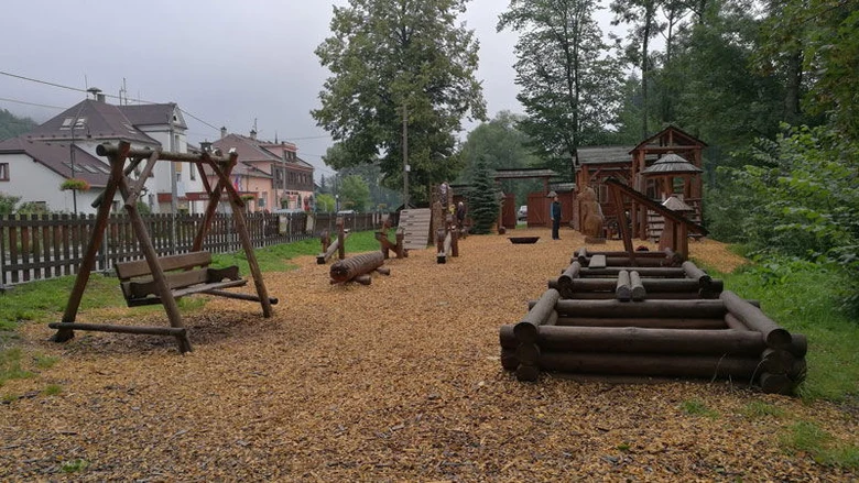 Dřevěné hřiště pro děti v přírodě s houpačkami a skluzavkami.