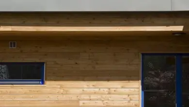 Dřevěná fasáda domu s modrými okny a venkovními kohouty.
